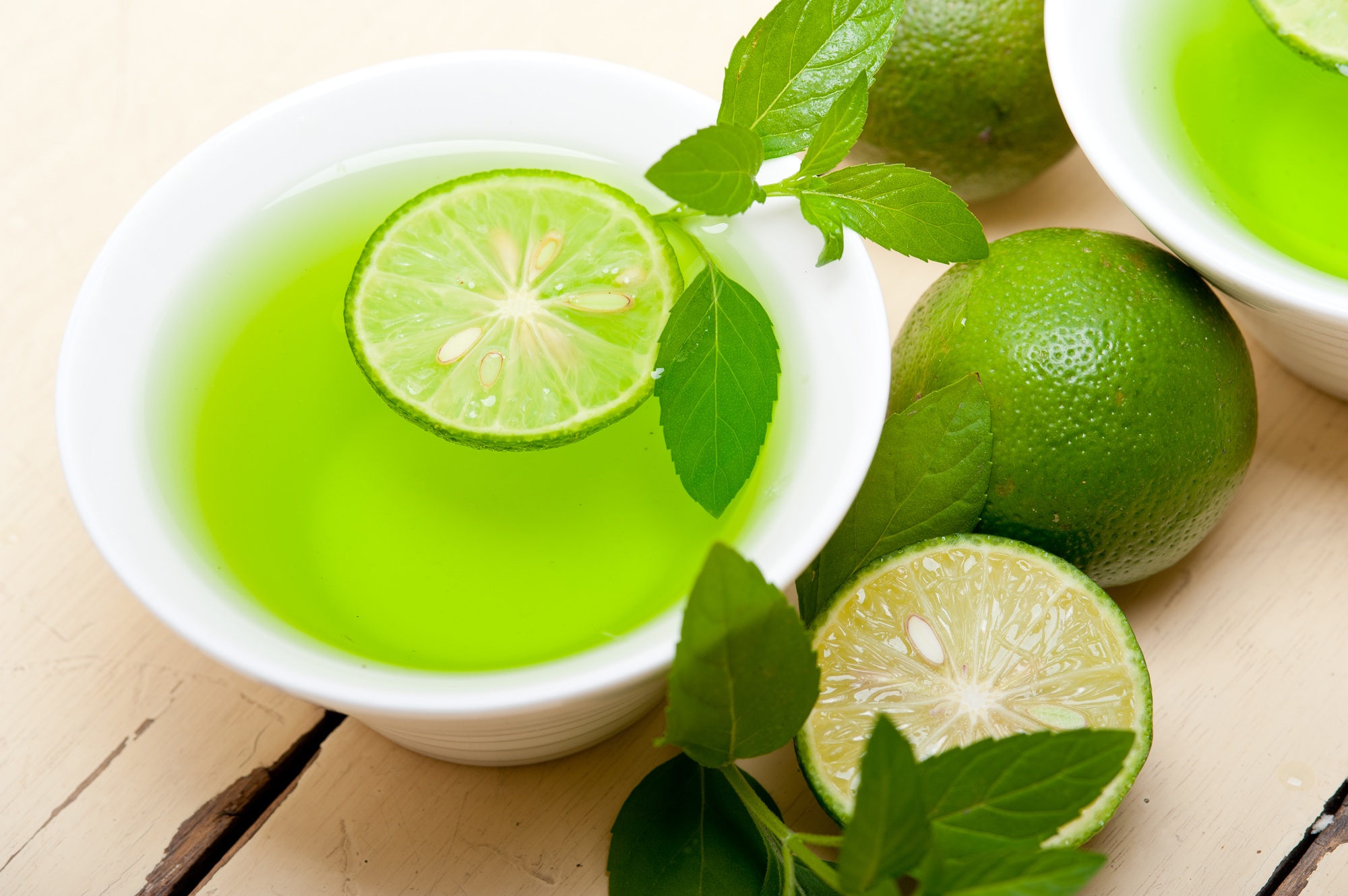 a bowl of green liquid with limes and leaves